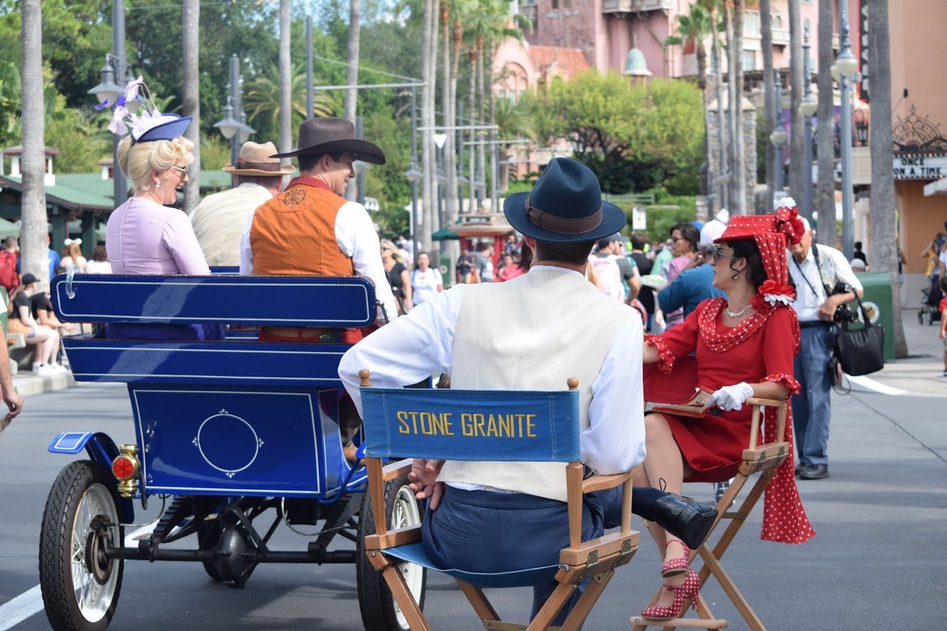 Disney's Citizens of Hollywood on Sunset Boulevard. Stone Granite and Flora Fiera are in directors chairs while Beau Wrangler and Evie Starlight drive by in an electric car.